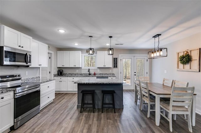 kitchen featuring hanging light fixtures, stainless steel appliances, white cabinetry, and a kitchen island