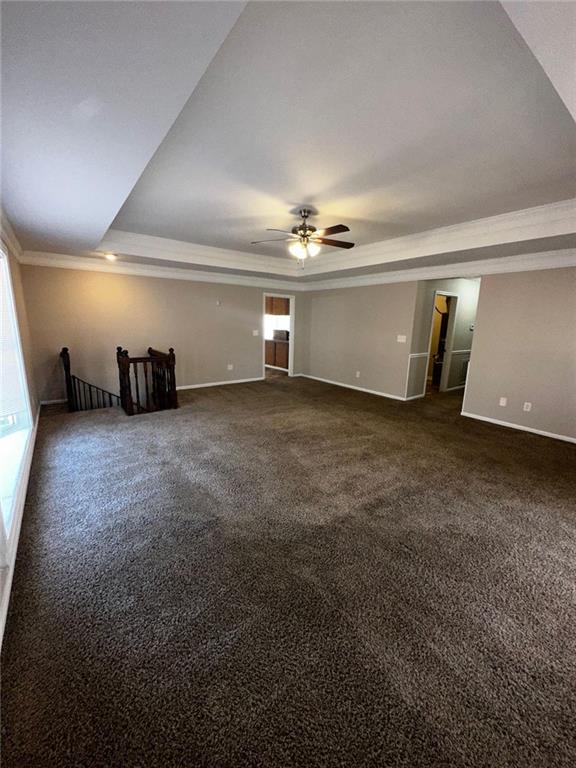 empty room featuring ceiling fan, plenty of natural light, a raised ceiling, and dark colored carpet