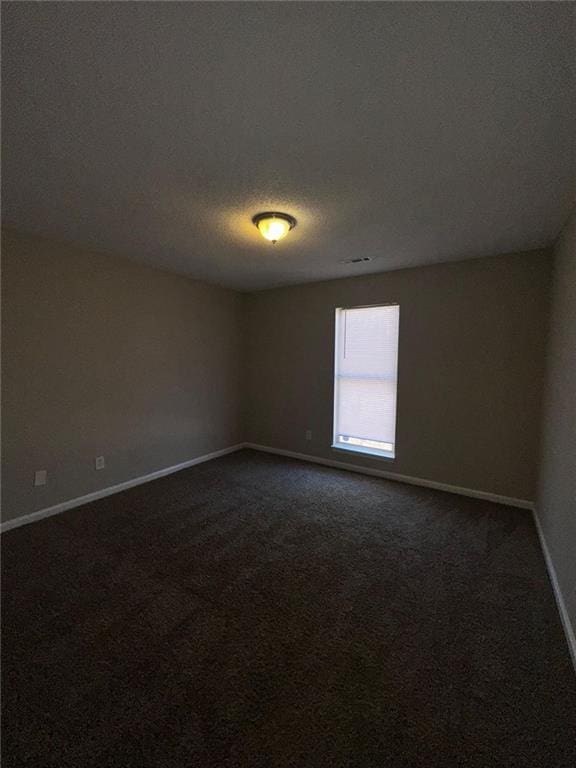 empty room with dark colored carpet and a textured ceiling