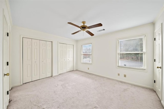 unfurnished bedroom with crown molding, light carpet, two closets, and ceiling fan