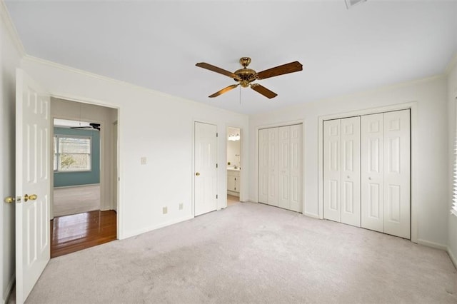 unfurnished bedroom with multiple closets, ceiling fan, crown molding, and light carpet