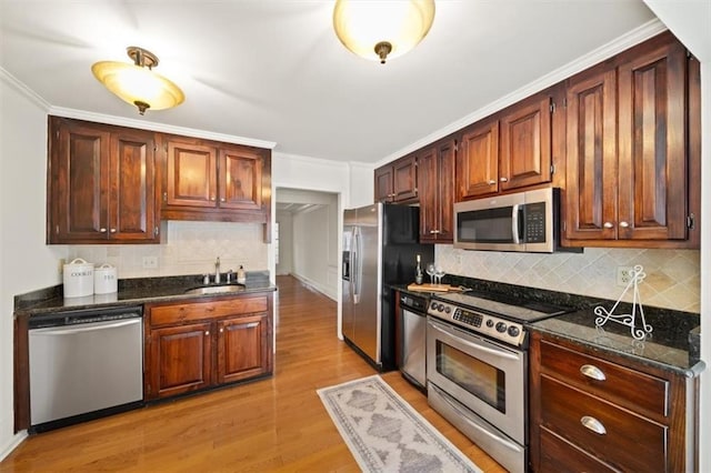 kitchen with appliances with stainless steel finishes, sink, dark stone counters, crown molding, and light wood-type flooring