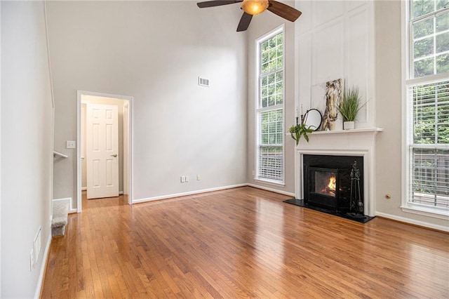 3710 Ridgefair Dr, Cumming, GA 30040 - unfurnished living room with a high ceiling, hardwood / wood-style flooring, healthy amount of natural light, a warm lit fireplace, and ceiling fan