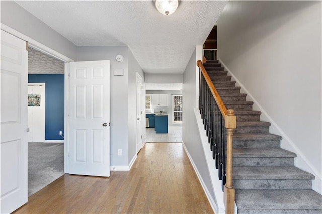 staircase with a healthy amount of sunlight, a textured ceiling, and wood-type flooring