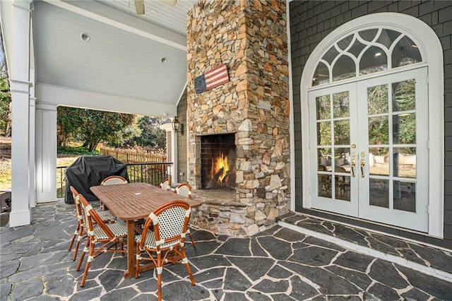 view of patio / terrace with fence, french doors, an outdoor stone fireplace, outdoor dining space, and a grill