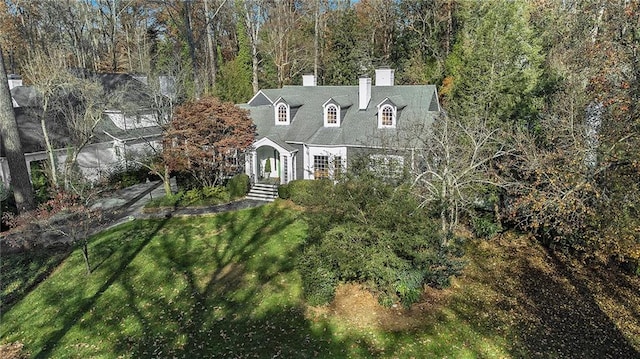 view of front of home with a chimney, a view of trees, and a front lawn