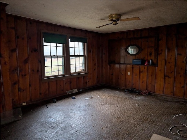 spare room with a textured ceiling, ceiling fan, and wood walls