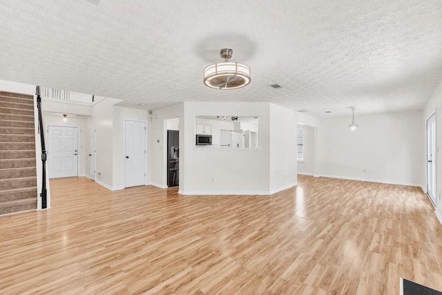 1186 Hawthorn Ln, Grayson, GA 30017 - unfurnished living room with a textured ceiling, light wood-style floors, stairway, and baseboards