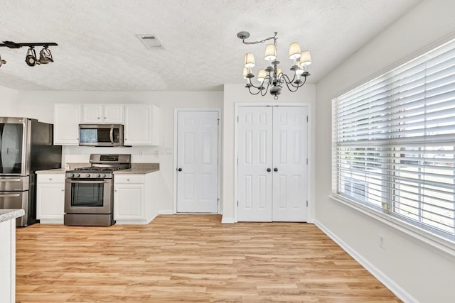 1186 Hawthorn Ln, Grayson, GA 30017 - kitchen with stainless steel appliances, a textured ceiling, a chandelier, white cabinetry, and light wood-style flooring