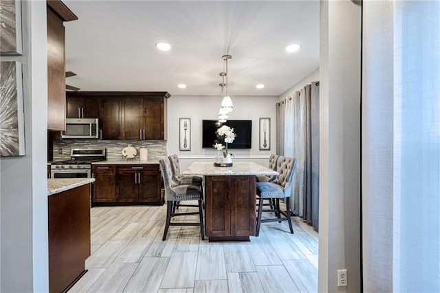 kitchen featuring recessed lighting, stainless steel appliances, a center island, a breakfast bar, and dark brown cabinets
