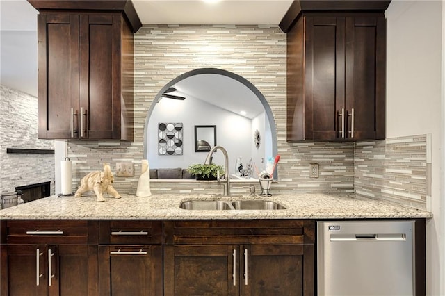 kitchen featuring dark brown cabinetry, stainless steel dishwasher, light stone counters, backsplash, and a sink