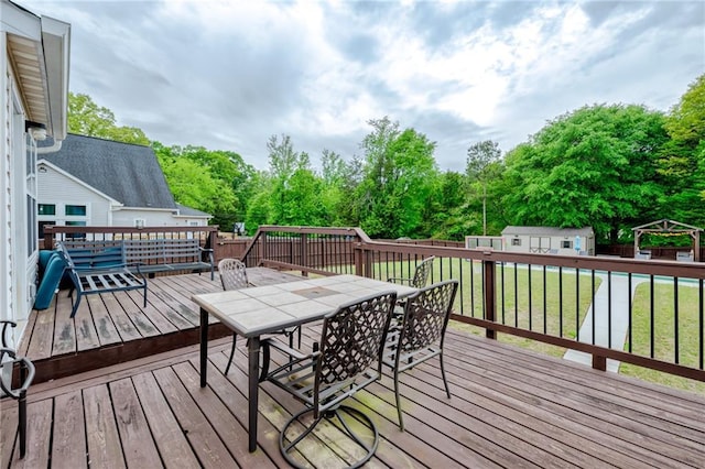 deck featuring fence, outdoor dining space, an outbuilding, and a yard