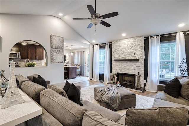 living area with light wood-style flooring, recessed lighting, vaulted ceiling, a ceiling fan, and a stone fireplace