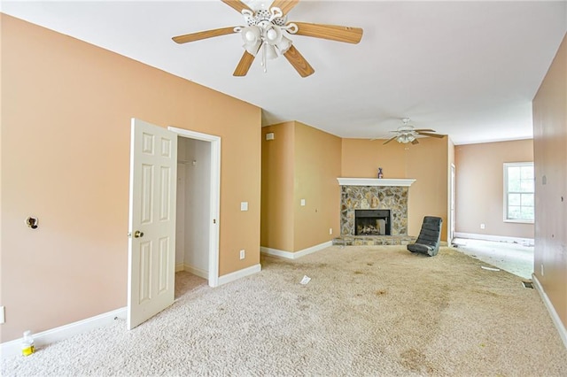 unfurnished living room featuring a stone fireplace, light carpet, and ceiling fan