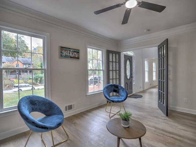 living area featuring hardwood / wood-style flooring, ceiling fan, a healthy amount of sunlight, and crown molding