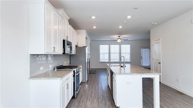 kitchen featuring stainless steel appliances, sink, white cabinets, light stone counters, and an island with sink