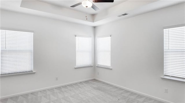 empty room with ceiling fan, light colored carpet, and a raised ceiling
