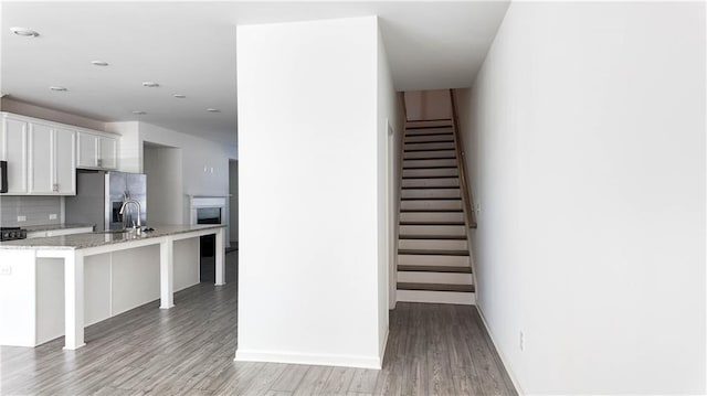 kitchen with white cabinets, a kitchen bar, decorative backsplash, light stone countertops, and stainless steel fridge