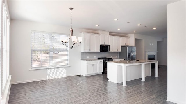kitchen featuring appliances with stainless steel finishes, pendant lighting, white cabinets, and a center island with sink