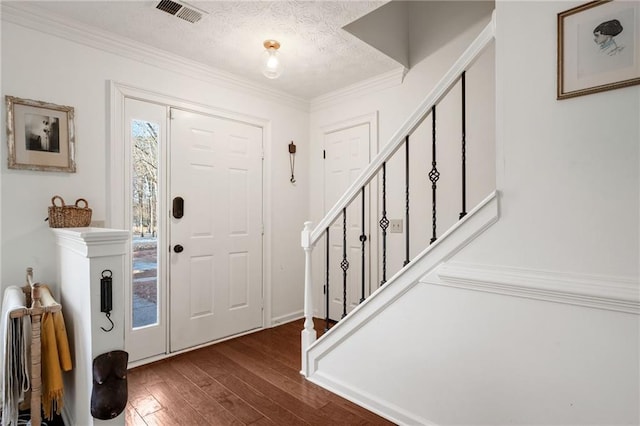 foyer entrance with dark hardwood / wood-style flooring, ornamental molding, and a textured ceiling