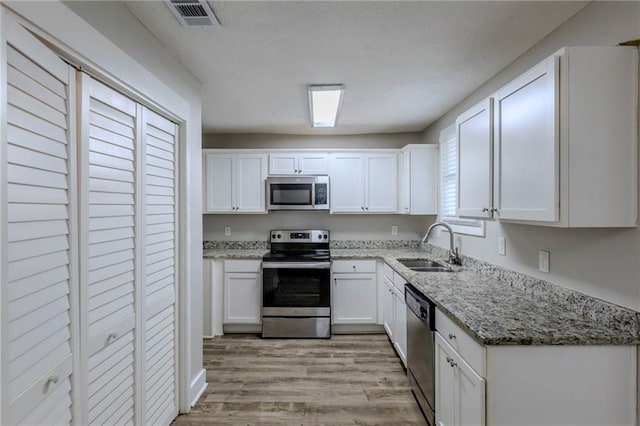 kitchen featuring white cabinets, appliances with stainless steel finishes, light stone countertops, and sink