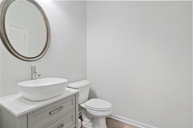 bathroom with toilet, vanity, wood finished floors, and baseboards