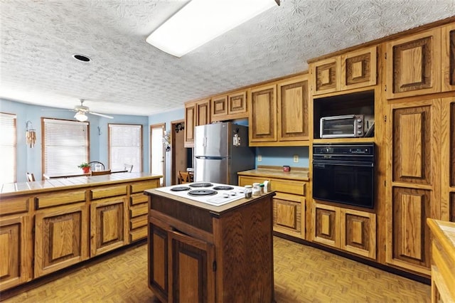 kitchen with tile counters, brown cabinetry, a center island, freestanding refrigerator, and oven