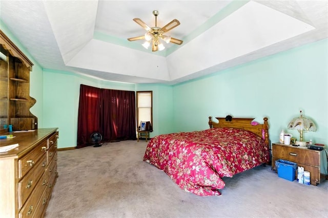 carpeted bedroom with a ceiling fan, a raised ceiling, and baseboards