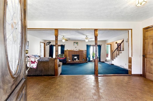 interior space featuring a ceiling fan, a brick fireplace, a textured ceiling, baseboards, and stairs