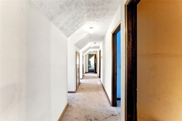 hallway featuring light carpet, vaulted ceiling, a textured ceiling, and baseboards