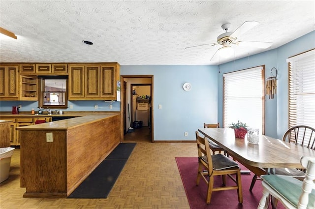 kitchen with baseboards, a ceiling fan, brown cabinets, a peninsula, and a textured ceiling