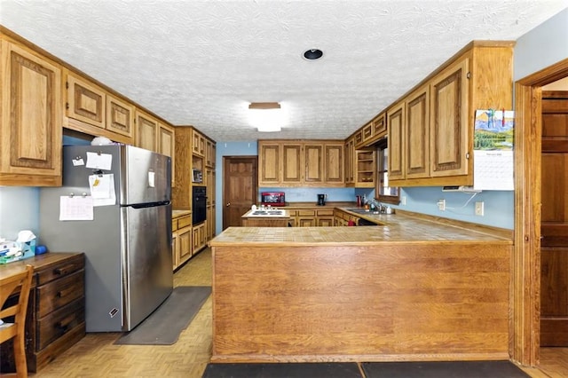 kitchen featuring brown cabinets, freestanding refrigerator, a sink, oven, and a peninsula