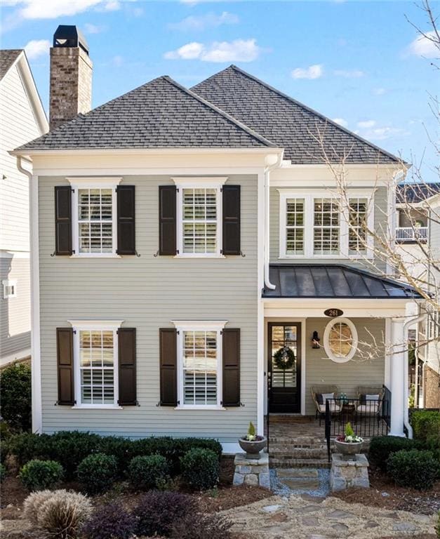 view of front of house with a standing seam roof, a chimney, a shingled roof, and metal roof