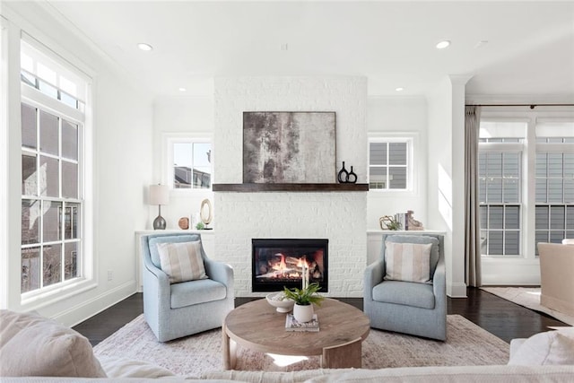 living area with recessed lighting, baseboards, a brick fireplace, and wood finished floors