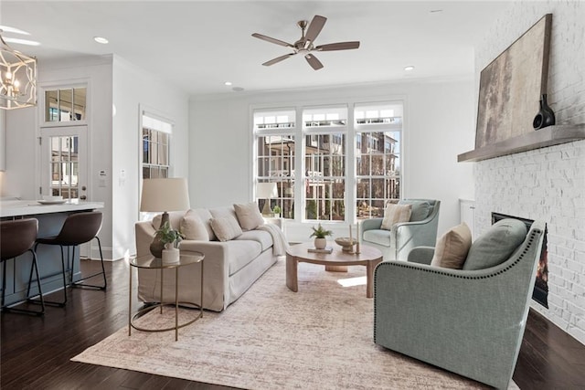 living room featuring crown molding, recessed lighting, a fireplace, ceiling fan with notable chandelier, and wood finished floors