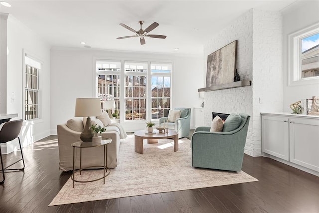 living area featuring a brick fireplace, ceiling fan, ornamental molding, recessed lighting, and dark wood-style floors