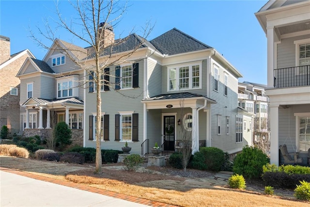 view of front of home featuring metal roof, roof with shingles, covered porch, and a chimney