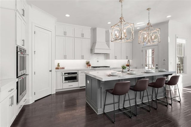 kitchen featuring dark wood-style floors, white cabinets, custom range hood, and a kitchen island with sink