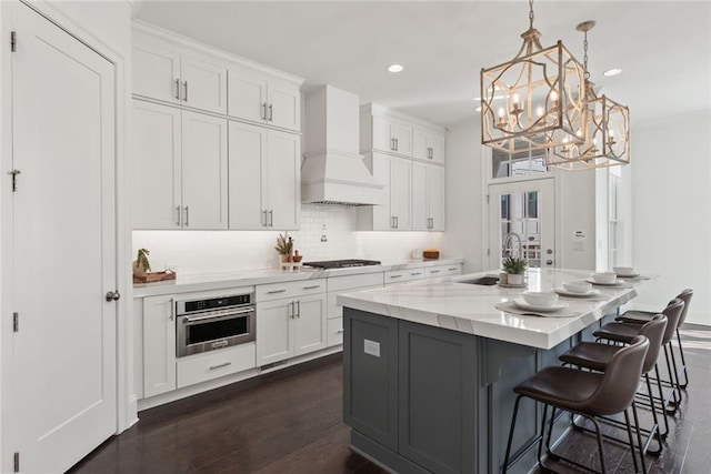 kitchen featuring stainless steel oven, a sink, white cabinetry, and premium range hood