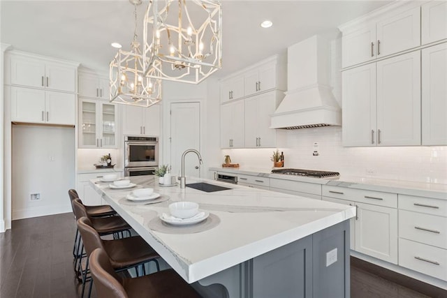 kitchen with backsplash, white cabinets, custom range hood, and a sink