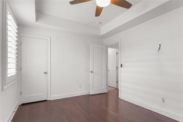 unfurnished bedroom with baseboards, a raised ceiling, wood finished floors, and a ceiling fan