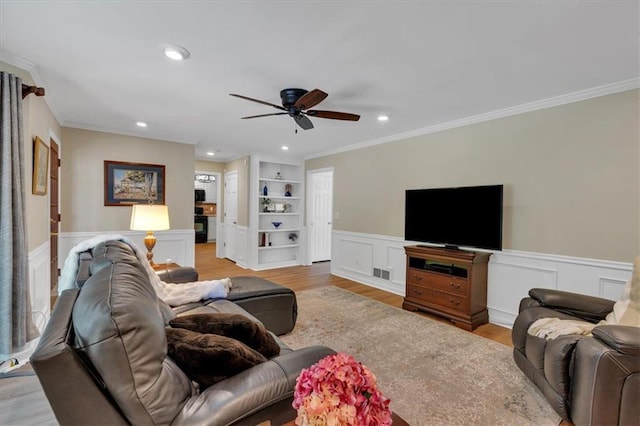 living room featuring visible vents, ornamental molding, ceiling fan, built in shelves, and light wood finished floors