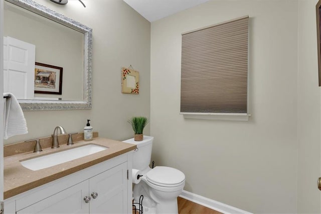 half bath with vanity, baseboards, toilet, and wood finished floors