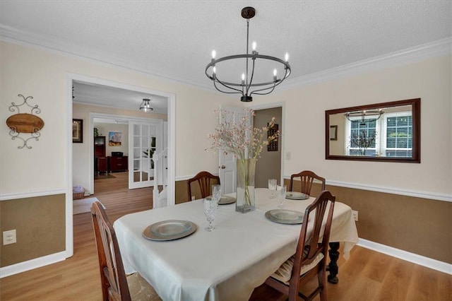dining space with a textured ceiling, wood finished floors, baseboards, an inviting chandelier, and ornamental molding