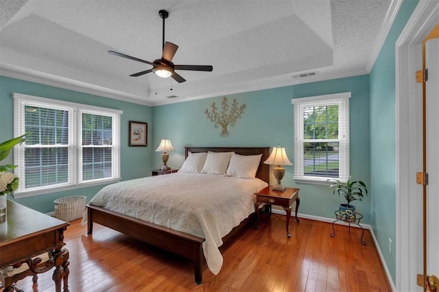 bedroom featuring visible vents, hardwood / wood-style floors, baseboards, a textured ceiling, and a tray ceiling
