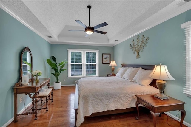 bedroom with crown molding, wood finished floors, baseboards, a textured ceiling, and a tray ceiling