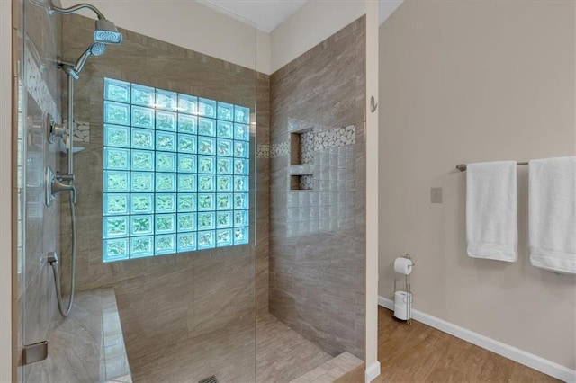 full bathroom featuring baseboards, a tile shower, and wood finished floors