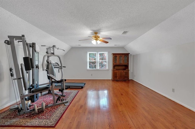 exercise room with ceiling fan, a textured ceiling, wood finished floors, lofted ceiling, and visible vents