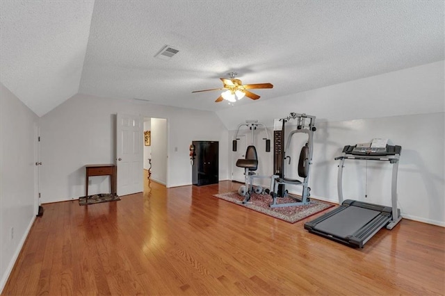 exercise room with visible vents, ceiling fan, wood finished floors, and vaulted ceiling