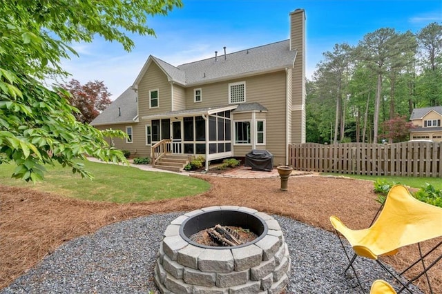 back of property featuring fence, a chimney, a sunroom, an outdoor fire pit, and a yard